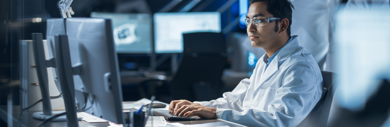 asian technician in white lab coat working on computer